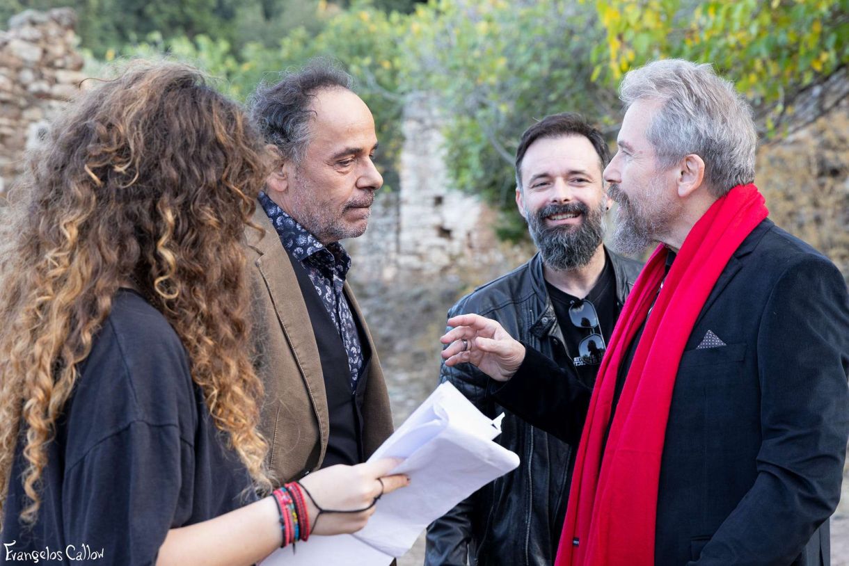Η ομάδα μιας παραγωγής συζητά σε εξωτερικό χώρο, με δύο άνδρες και μια γυναίκα στο πλάνο. Ο ένας άνδρας φοράει σακάκι και ο άλλος έχει γενειάδα. Η γυναίκα κρατάει σημειώσεις.