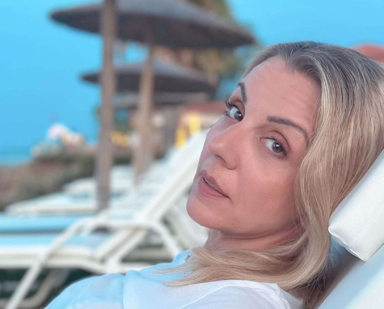 Η Ματίνα Νικολάου καθισμένη σε μια καρέκλα, με φόντο το ηλιοβασίλεμα και ξαπλώστρες στον κόλπο.