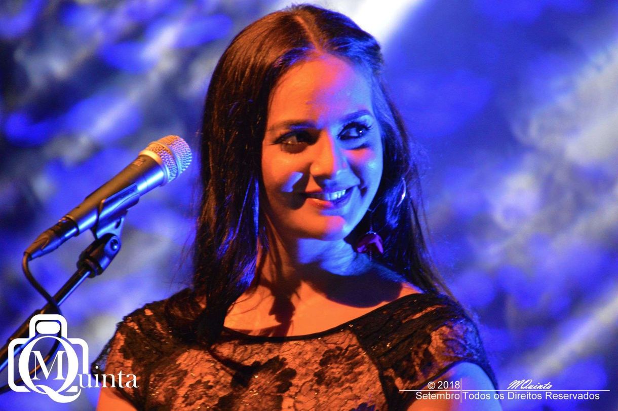 Close-up of a woman smiling on stage, microphone in front of her, with blue lighting creating a vibrant atmosphere.